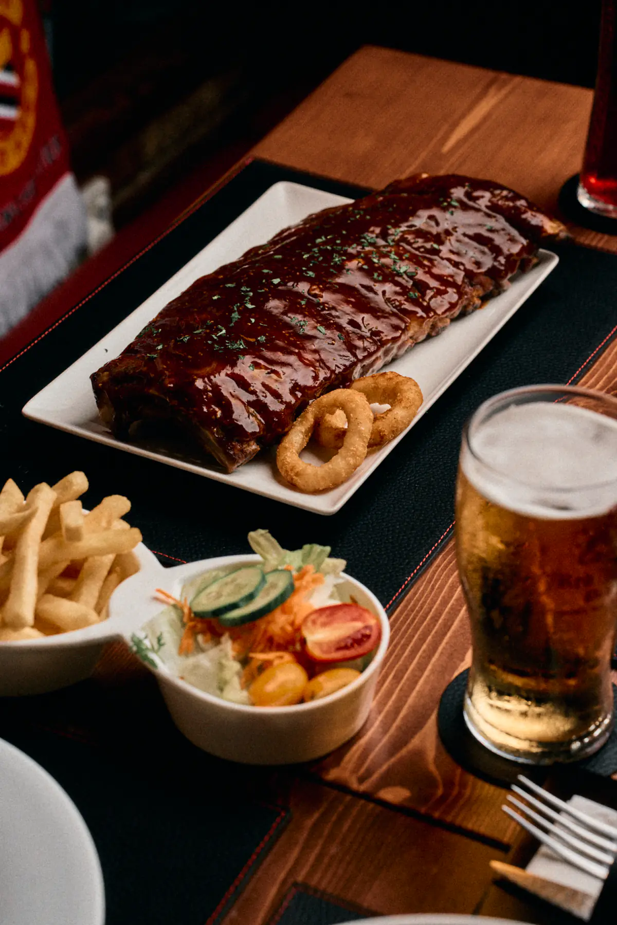 A rack of glazed ribs with onion rings, chips and a side salad, a pint of lager beside